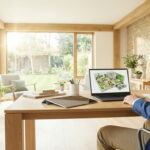 Man viewing 3D architectural rendering on laptop in a bright, modern living room with large windows and natural light.