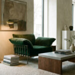 A sophisticated modern interior featuring an emerald velvet armchair, concrete coffee table, gold lamp, and abstract art.