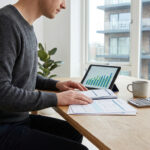 Homme travaillant à une table sur ses documents de copropriété et une tablette affichant un graphique.