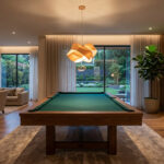 Un salon spacieux et moderne avec un billard central, un coin salon et de grandes baies vitrées donnant sur un jardin.